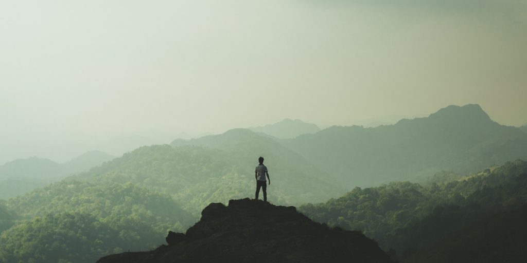 Young man stands at top of hill looking out over forests