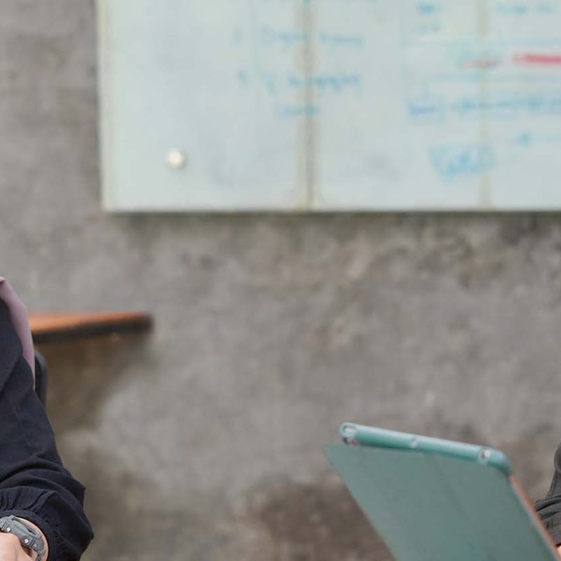 Two Asian women wearing hijabs talking to each other in office.