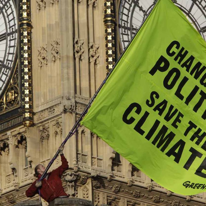 Greenpeace Activist in front of Big Ben with banner saying "Change the Politics, Save the Climate"