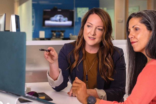 Two business women talking about sales in office at desk with laptop
