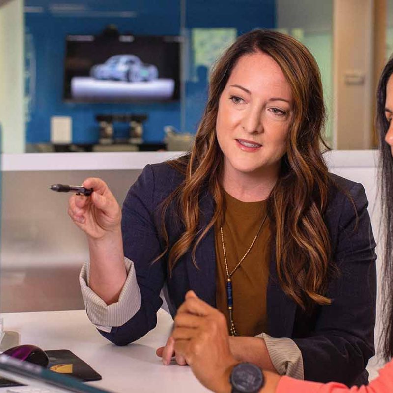 Two business women talking about sales in office at desk with laptop