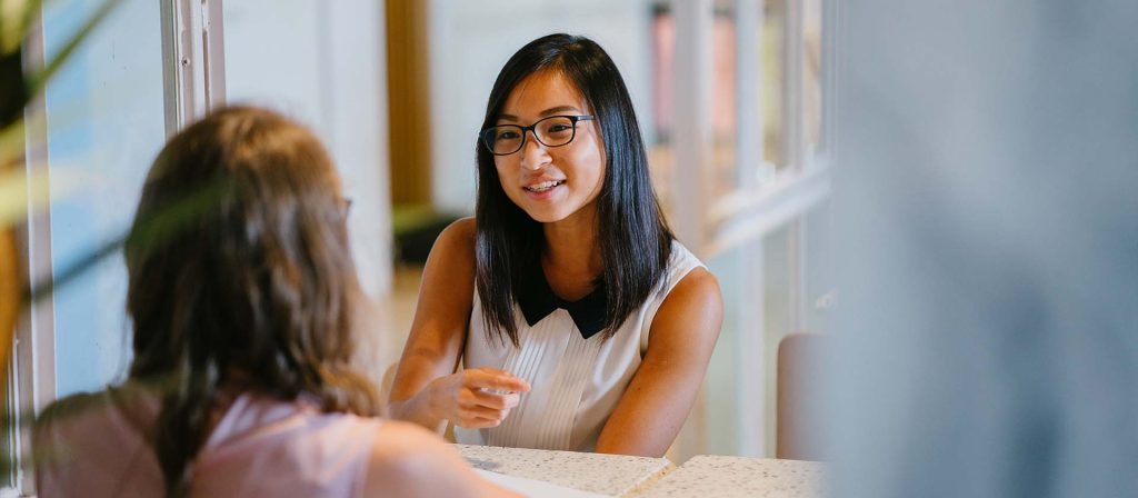 Two women are having a conversation whilst sitting across from each other at a table