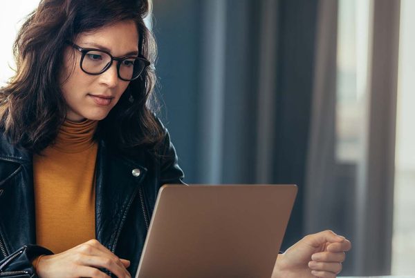 A woman sitting at a desk, looking at the screen of her laptop