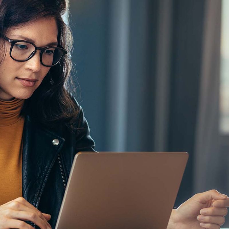 A woman sitting at a desk, looking at the screen of her laptop