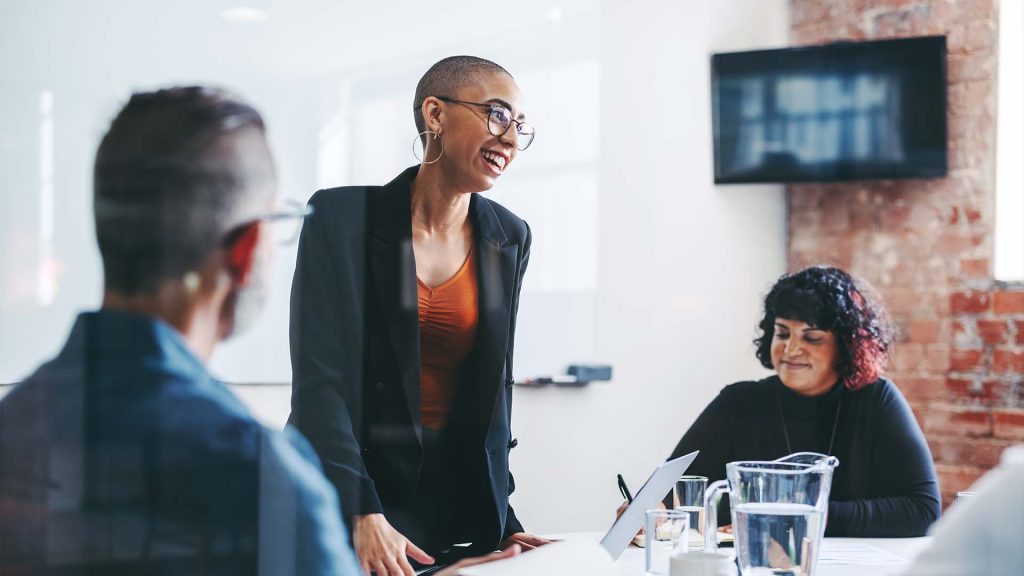 Women smiling while presenting in meeting with male and female colleague