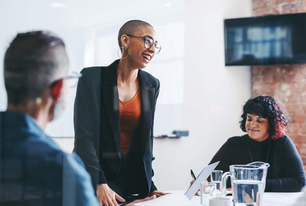 Women smiling while presenting in meeting with male and female colleague