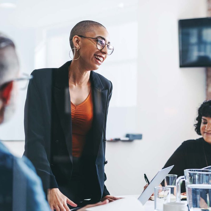 Women smiling while presenting in meeting with male and female colleague